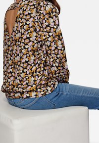 Blusa nera a fiori con motivi multicolori, dotata di un dettaglio a chiave sul retro, abbinata a jeans blu. Tessuto morbido e leggero.