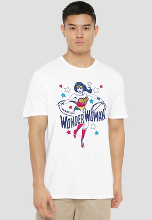 Young man wearing a white t-shirt with a colorful Wonder Woman graphic and text, standing against a plain light gray background.