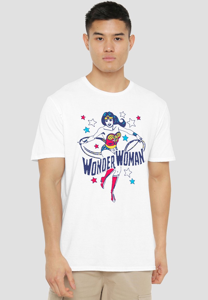 Young man wearing a white t-shirt with a colorful Wonder Woman graphic and text, standing against a plain light gray background.