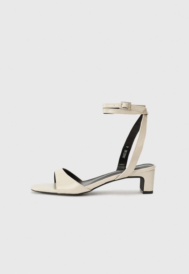 Sandales à talons beiges avec une sangle cheville et un détail de boucle. Matière en cuir lisse, bout ouvert et design de talon carré.