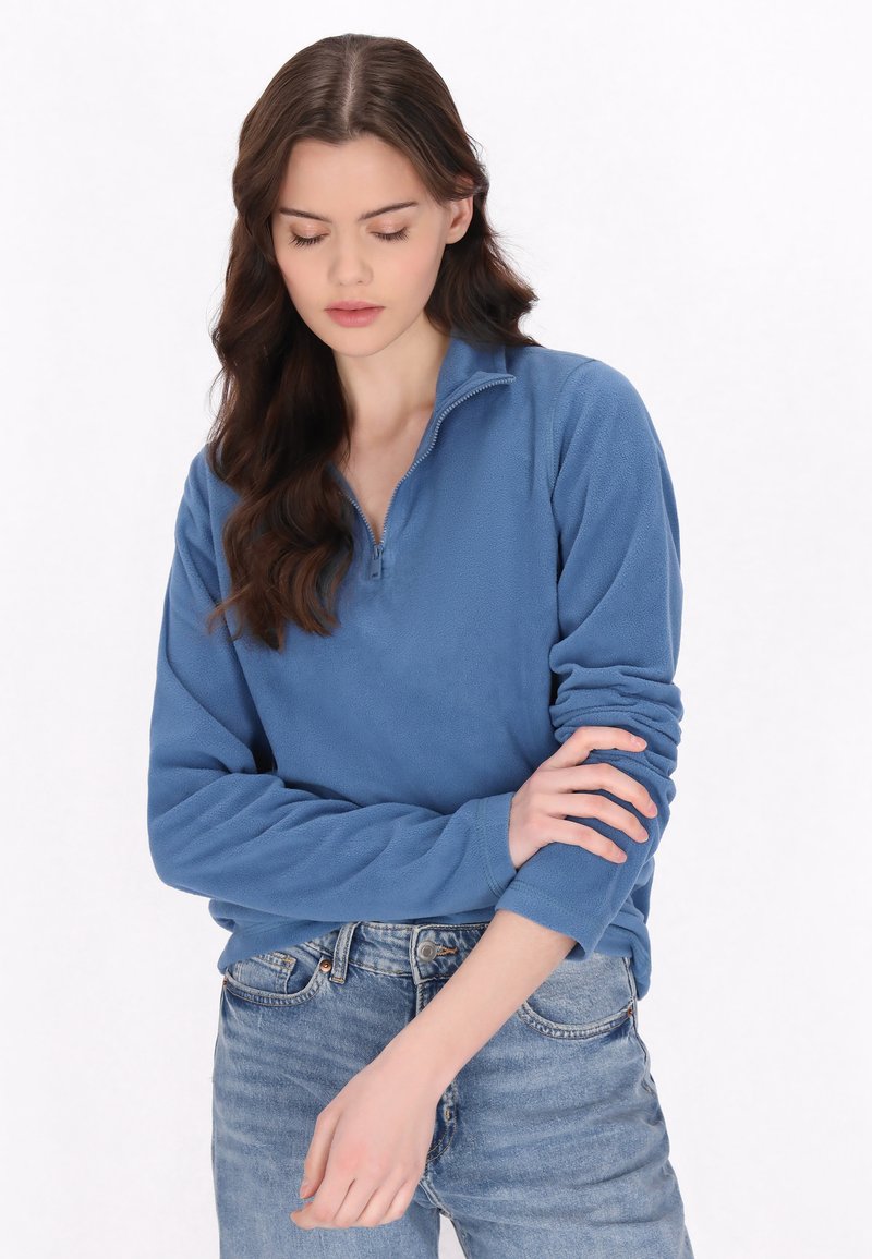 Pullover in fleece azzurro chiaro con colletto a metà zip, maniche lunghe e texture morbida. Indossato con jeans azzurri chiari. Nessun motivo o dettaglio visibile.