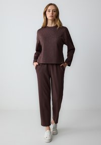 Bruine, lange mouwen top met studdetails, gecombineerd met bijpassende losse broek en witte sneakers. Gladde stof, casual ontwerp.