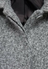 Manteau en laine gris avec une surface texturée, doté d'un col pointu et d'une fermeture avant à un seul bouton gris. Doublure intérieure visible.