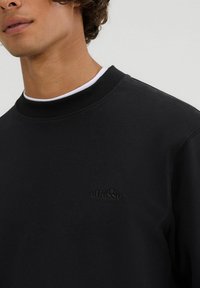 Schwarzer Sweatshirt mit geripptem Kragen und subtil gesticktem Logo. Weiche Textur und lässiges Design, mit bequemem Schnitt.