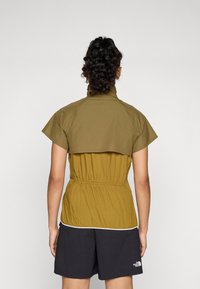Short-sleeve, olive green jacket with a high collar and elastic waist, worn over black shorts. Smooth, lightweight fabric with minimal seams.