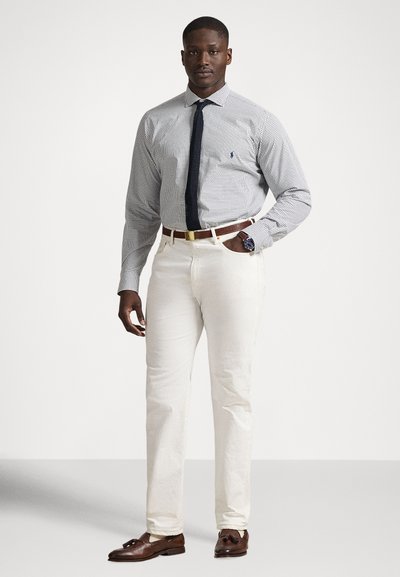 Πουκάμισο με κουμπιά και μοτίβο καρό σε μπλε και λευκό, ναυτικό μπλε γραβάτα, κρεμ παντελόνι και καφέ δερμάτινα μοκασίνια. Χρυσός ζωνάρι ως λεπτομέρεια.