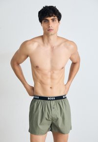 Zöld boxeralsó fekete "BOSS" logós derékpánttal, gombos záródással és puha, sima textúrával. Modellen viselve.
