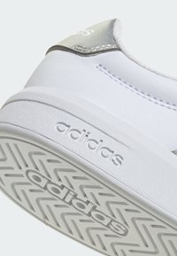 Weiße Adidas-Sneaker-Ferse mit strukturierter Sohle, auf der Seite und unten das Adidas-Logo geprägt ist, sowie grauer Fersenlasche mit Logo.
