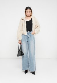 Κρεμ ψεύτικο γούνινο μπουφάν cropped με κουκούλα, μαύρο κοντομάνικο μπλουζάκι, ανοιχτού μπλε ψηλόμεσα τζιν και μια μικρή μαύρη τσάντα, συνδυασμένο με μυτερές γόβες.