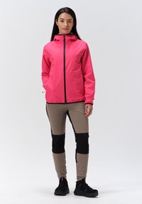 Rosa vattentät jacka med blixtlås, långa ärmar och huva; kombinerad med beiga och svarta åtsittande byxor. Svarta träningsskor fulländar outfiten.