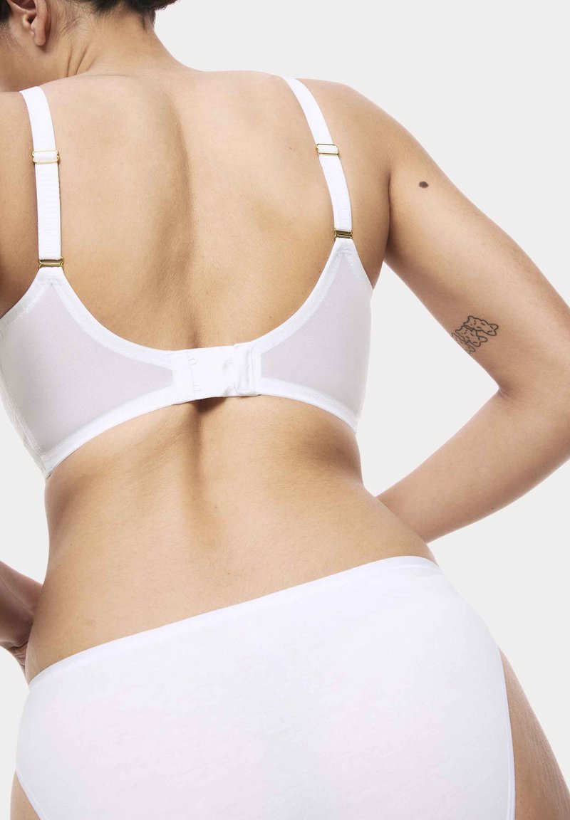 Witte beha met verstelbare banden, haak-en-oogsluiting, een gladde textuur en minimale ontwerpdetails. Witte slip met eenvoudige snit en stof.