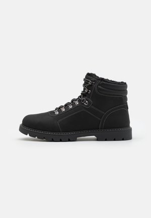 Botte d'hiver en cuir noir avec cheville rembourrée, œillets métalliques, doublure en fourrure, semelle en caoutchouc épaisse et semelle crantée, vue de côté.