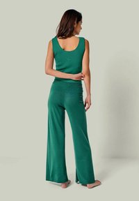 Smaragdgrünes, geripptes Stricktanktop kombiniert mit passenden weit geschnittenen Hosen. Verfügt über einen runden Ausschnitt am Rücken, eine weiche Textur und dezente seitliche Schlitze an den Hosen.