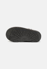 Suela de zapato de goma negra con un diseño de relieve y un logo UGG en relieve, con un diseño ancho y plano y una superficie texturizada para mayor agarre.