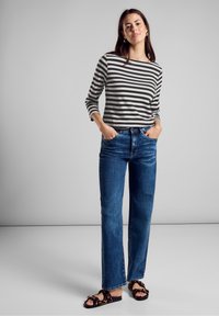 Pasiasta bluzka z długim rękawem w czerni i bieli, zestawiona z niebieskimi dżinsami o prostym kroju. Obuwie ma wzór w panterkę z ciekawym detalem.