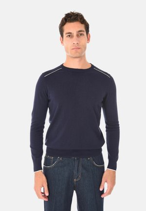 Maglione lavorato a maglia blu navy con maniche lunghe e scollatura a girocollo, caratterizzato da un bordo a contrasto nelle cuciture delle spalle. Abbinato a jeans di denim scuro.