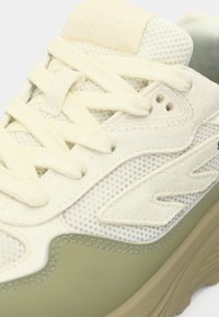 Gaiši zaļa un krēmīga sneaker kurpes ar tīkla un zamšādas augšdaļu, plakaniem aukliņām un biezu bēša gumijas zolīti. Akcentētas ar logotipu.