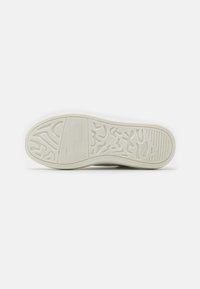 Hvid sneakersål med tekstureret gummi, der har et bølgemønster og vandrette riller. Flad design, tyk kant for stabilitet.