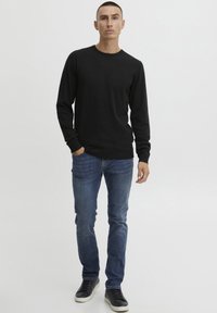 Fekete, hosszú ujjú, kereknyakú pulóver kék, skinny farmernadrággal és fekete sportcipővel párosítva. Egyszerű dizájn, sima textúra, minimalista részletezés.