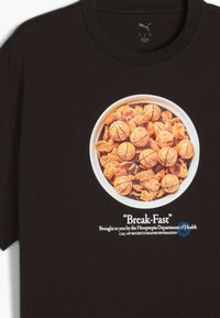 T-shirt noir avec un graphique d'un bol de céréales rempli de morceaux de céréales bruns et de morceaux en forme de ballon de basket orange, étiqueté "Break-Fast".