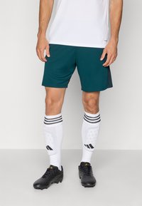 Pantalones cortos deportivos en verde azulado con un acento negro, combinados con calcetines blancos con rayas negras y un diseño estampado, complementados con botas de fútbol negras.
