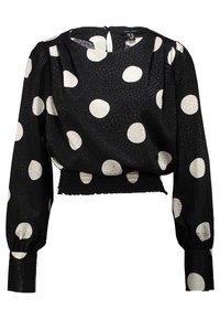 Blouse noire à manches longues avec de grands pois blancs et un tissu texturé. Taille cintrée avec une ouverture au niveau de la nuque dans le dos.