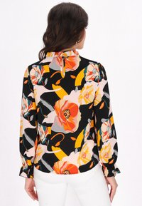 Blommig blus i svart, med stora orange och rosa blommor. Långa ärmar med samlade manschetter och en snörning i nacken. Slätt tyg.