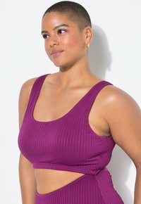 Pružný fialový crop top s širokými ramínky a výřezem v pase, vyrobený z elastického materiálu, s přiléhavým střihem.