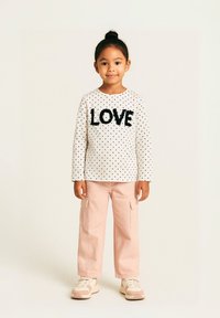 Haut à manches longues blanc avec des pois noirs et un lettrage texturé "LOVE", associé à un pantalon cargo rose et des baskets claires.