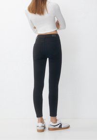 Jeans skinny neri con vita media, caratterizzati da una texture liscia, tasche posteriori standard e abbinati a sneakers bianche.