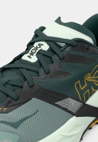 Chaussure de course Hoka avec une tige en mesh bleu sarcelle et noir, des accents texturés, une semelle rembourrée et des lacets ton sur ton pour un maintien sécurisé.