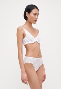 Weißes Spitzen-Bralette mit floralen Mustern und gewellten Kanten, kombiniert mit passenden weißen Spitzenunterhosen, die ein ähnliches Design und eine ähnliche Textur aufweisen.