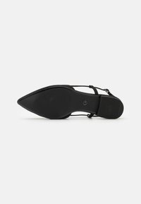 Black pointed-toe shoe with a flat sole, featuring a textured rubber bottom, ankle strap, and smooth upper material. Simple design.