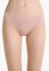 Vrouw in lichtroze naadloze hipsteronderbroek, weergegeven van taille tot bovenste dijen op een witte achtergrond.