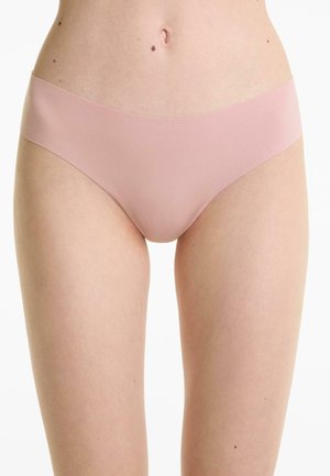 Vrouw in lichtroze naadloze hipsteronderbroek, weergegeven van taille tot bovenste dijen op een witte achtergrond.