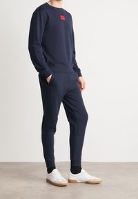 Felpa color blu navy e pantaloni coordinati in tessuto morbido, con un patch logo rosso sul petto, dotati di polsini e cintura elastici.