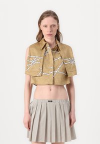 Camicia dorata a maniche corte con motivi a nastro bianco a contrasto. Indossata su una gonna bianca a pieghe con pois.