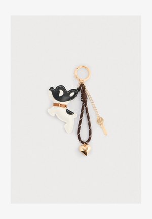 Portachiavi con un design di un cane bianco e nero realizzato in pelle, con una cinghia marrone, hardware dorato, un charm a forma di cuore e una chiave attaccata.