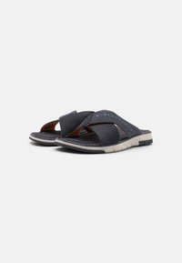 Marineblaue Sandalen mit überkreuzten Riemen aus strukturiertem Stoff. Mit einer grauen Gummisohle und dezentem Branding am Riemen.