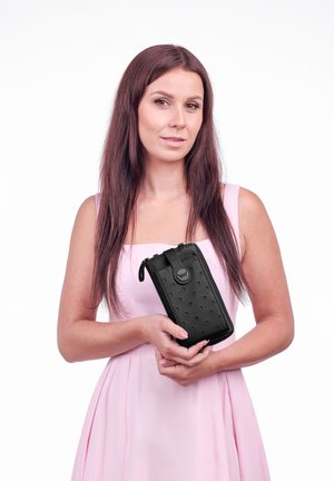 Černá peněženka na zip vyrobená z texturovaného materiálu s tečkovaným vzorem a kulatým logem, držena na klasickém bílém pozadí.