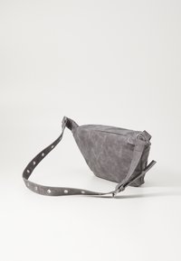 Grå crossover-veske laget av teksturert materiale, med flat form, justerbar stropp med sirkulære utskjæringer og minimalistisk design.