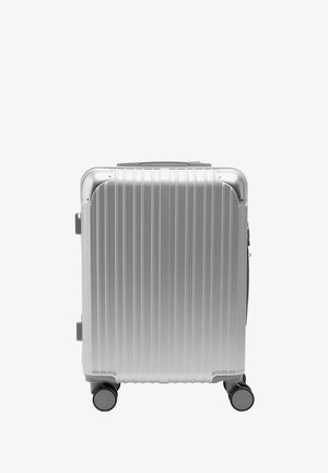 Srebrna walizka z twardą skorupą z pionowymi żebrowaniami, podwójnymi kółkami i solidnym zamkiem błyskawicznym. Posiada górny uchwyt oraz wzmocnione narożniki.