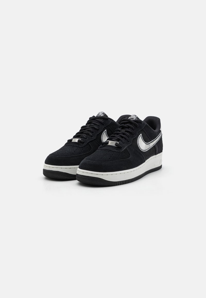 Zwarte suède sneakers met witte accenten, ronde neus, dikke zool, gestructureerde grip en geperforeerde details aan de voorkant.