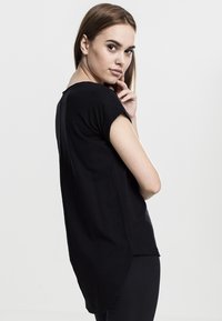 Haut noir à manches courtes en tissu doux, avec un ourlet arrondi et une coupe décontractée, mettant en avant une texture lisse et un design minimaliste.