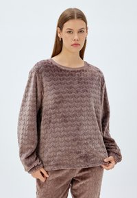 Pehmeä, mauve-sävyinen neulepaita, jossa on kohotettu zigzag-kuvio, pyöreä pääntie ja pitkät hihat, jotka on varustettu joustavilla hihansuilla ja helmakäänteellä.