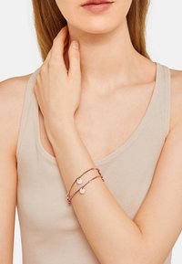 Bracelet en or rose avec deux charms circulaires, présentant un design de chaîne délicate et superposée. Texture lisse, style minimaliste.