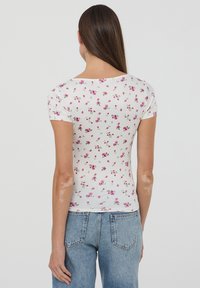 Top bianco a maniche corte con un motivo floreale in rosa e verde. Design aderente con scollatura a barchetta e tessuto leggero e morbido.