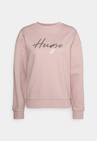 Helle rosa Sweatshirt aus weichem Stoff mit Rundhalsausschnitt und gerippten Bündchen. Auf der Vorderseite befindet sich ein graues und weißes, geschwungenes "Hugo"-Logo.