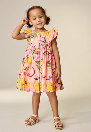 Florales Kinderkleid in Pink mit Fruchtmustern, Rüschenärmeln, Knopfleiste und einem gerafften Rock; kombiniert mit beigen Sandalen mit Stickerei.