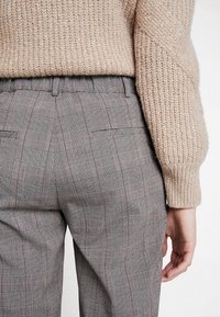 Grå rutig byxor med en subtil röd accent, med en synlig tygtextur; kombinerat med en beige stickad tröja.